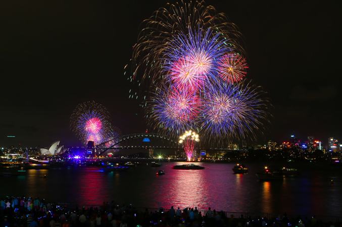 Fireworks exploding over the Sydney skyline at night, with the Harbour Bridge and city lights in view.