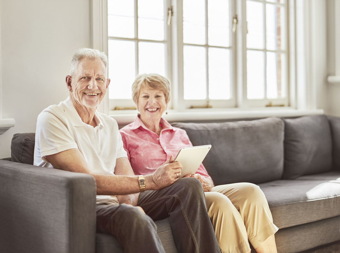A mature couple sitting on a couch with a laptop open in front of them