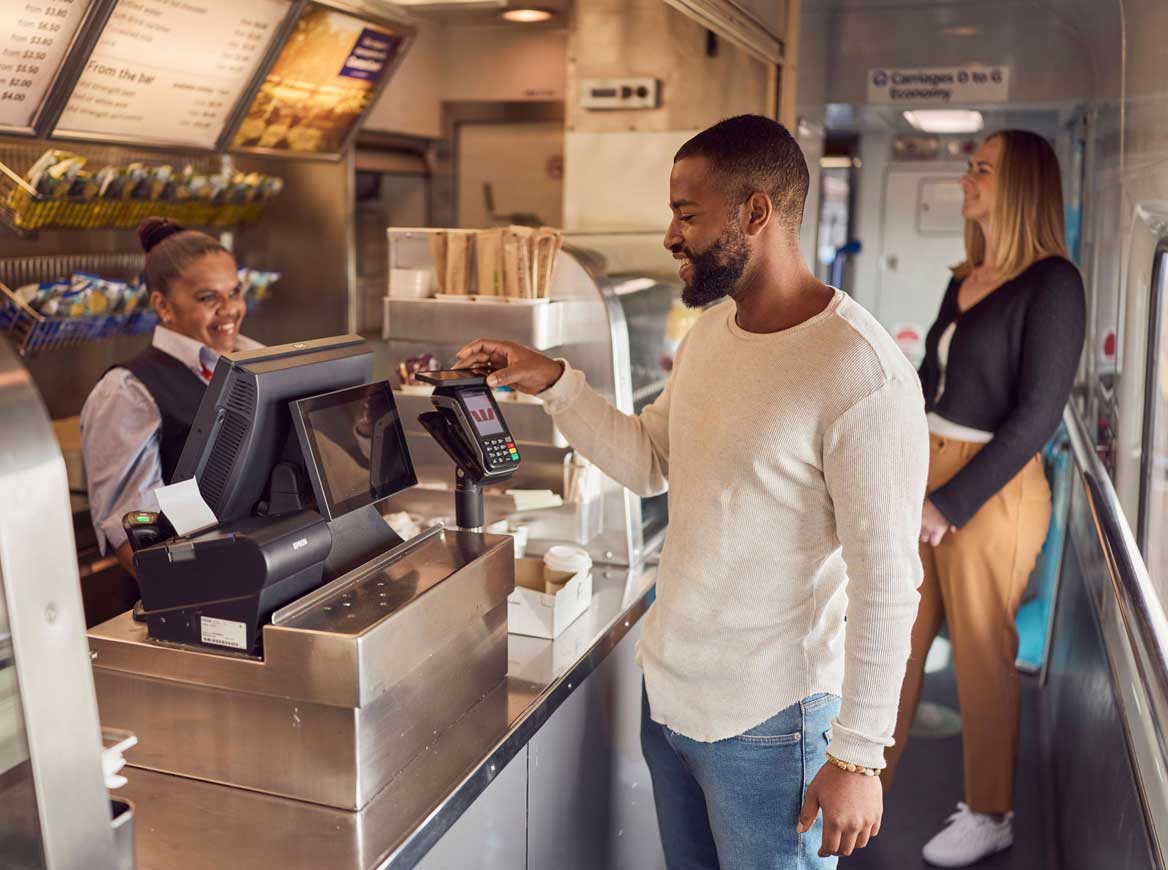 A male customer taps his phone to pay for a coffee at the buffet car onboard a train.